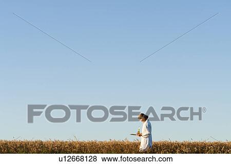 Stock Photo - Woman in lab coat beside field, Manitoba, Canada. Fotosearch