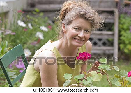 Woman in mid 50s seated in garden holding geranium, Manitoba, Canada View Large Photo Image Stock Image - Woman in mid 50s seated in garden holding geranium, Manitoba, Canada. Fotosearch