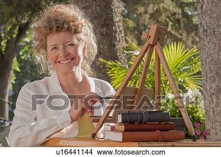 Woman in mid 50's seated outdoor with small painting easel, Manitoba, Canada View Large Photo Image Picture - Woman in mid 50's seated outdoor with small painting easel, Manitoba, Canada. Fotosearch