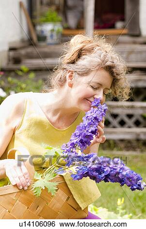 Stock Photograph - Woman in mid-50's smelling flowers in backyard garden, Manitoba, Canada. Fotosearch