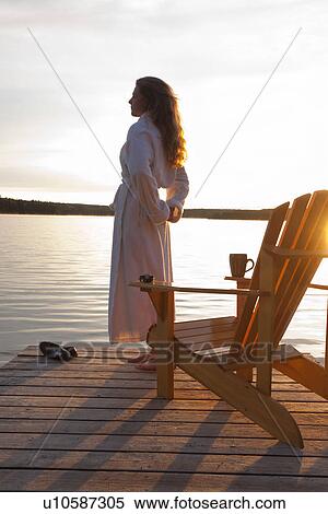 Stock Photography - Woman in robe standing on dock at sunrise, Clear Lake, Manitoba, Canada. Fotosearch