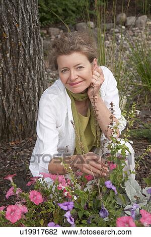 Stock Image - Woman kneeling beside flowers in garden, Manitoba, Canada. Fotosearch