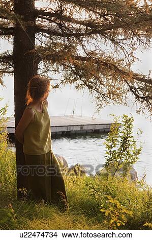 Woman leaning against tree looks over lake, Clear Lake, Riding Mountian National Park, Maniotba, Canada View Large Photo Image Picture - Woman leaning against tree looks over lake, Clear Lake, Riding Mountian National Park, Maniotba, Canada. Fotosearch