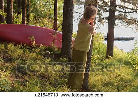 Stock Image - Woman leaning against tree looks over lake, Clear Lake, Riding Mountian National Park, Maniotba, Canada. Fotosearch