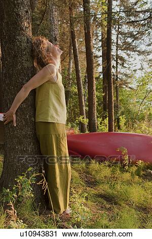 Stock Image - Woman leaning against tree reaching backward to touch tree, Clear Lake, Manitoba. Fotosearch