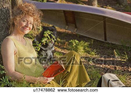 Woman leans against tree reading book, with dog, Clear Lake, Riding Mountain National Park, Manitoba, Canada View Large Photo Image Stock Image - Woman leans against tree reading book, with dog, Clear Lake, Riding Mountain National Park, Manitoba, Canada. Fotosearch