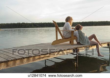 Picture - Woman seated in deck chair does hair of woman seated on dock, Clear Lake, Manitoba, Canada. Fotosearch