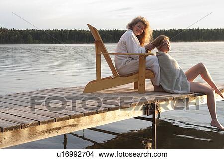 Woman seated in deck chair does hair of woman seated on dock, Clear Lake, Manitoba, Canada View Large Photo Image Picture - Woman seated in deck chair does hair of woman seated on dock, Clear Lake, Manitoba, Canada. Fotosearch