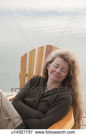 Stock Photo - Woman seated in deck chair on dock with eyes closed, Clear Lake, Manitoba, Canada. Fotosearch