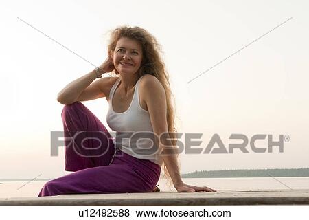 Stock Photo - Woman seated on dock by Clear Lake, Manitoba, Canada. Fotosearch
