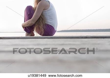 Stock Photo - Woman seated on dock by Clear Lake, Manitoba, Canada. Fotosearch