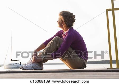 Stock Photo - Woman seated on dock, Clear Lake, Manitoba, Canada. Fotosearch