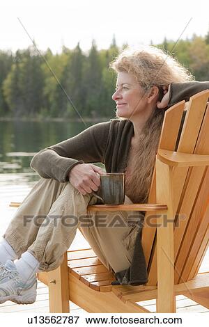 Woman seated sideways in deck chair holding mug, Clear Lake, Manitoba, Canada View Large Photo Image Stock Photo - Woman seated sideways in deck chair holding mug, Clear Lake, Manitoba, Canada. Fotosearch