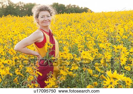 Stock Image - Woman standing in field of yellow flowers, Manitoba, Canada. Fotosearch