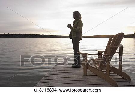Woman standing on dock holding cup of coffee at sunset, Clear Lake, Manitoba View Large Photo Image Picture - Woman standing on dock holding cup of coffee at sunset, Clear Lake, Manitoba. Fotosearch