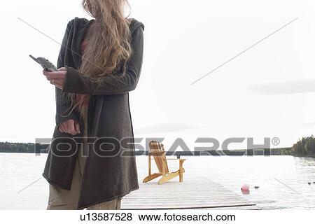 Stock Photo - Woman using cell phone, deck chair on dock, Clear Lake, Manitoba, Canada. Fotosearch