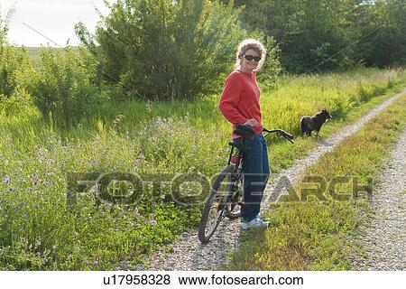 Stock Photo - Woman with bicycle on country road with dog, Manitoba, Canada. Fotosearch