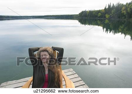 Woman with eyes closed seated in deck chair on dock beside Clear Lake, Riding Mountain National Park, Manitoba, Canada View Large Photo Image Stock Image - Woman with eyes closed seated in deck chair on dock beside Clear Lake, Riding Mountain National Park, Manitoba, Canada. Fotosearch