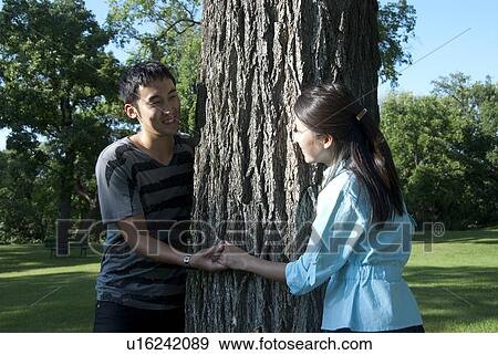 Young couple hold hands around tree in Assiniboine Park, Winipeg, Canada View Large Photo Image Stock Photo - Young couple hold hands around tree in Assiniboine Park, Winipeg, Canada. Fotosearch