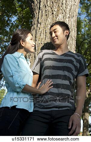 Stock Image - Young couple stand beside tree in Assiniboine Park, Winnipeg, Canada. Fotosearch