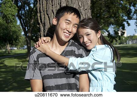 Stock Image - Young couple stand beside tree in Assiniboine Park, Winnipeg, Canada. Fotosearch