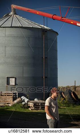 Stock Image - Young farmer stands in front of grain bin in farmyard, Redvers, Saskatchewan, Canada. Fotosearch