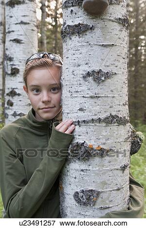 Stock Photo - Young girl with arm around tree, Manitoba, Canada. Fotosearch
