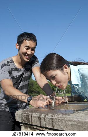 Picture - young man assists young women at water fountain, Assiniboine Park, Winnipeg, Caada. Fotosearch