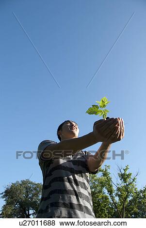 Stock Photo - Young man holding seedling with outstretched arms, Assiniboine Park, Winnipeg, Canada. Fotosearch