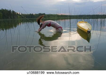 Stock Photo - Young woman diving into water, beside kayak, Lake Katherine, Riding Mountain National Park, Manitoba, Canada. Fotosearch