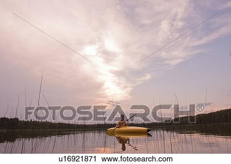 Stock Image - Young woman in kayak dwarfed by sky at sunset, Lake Katherine, Riding Mountain National Park, Manitoba, Canada. Fotosearch