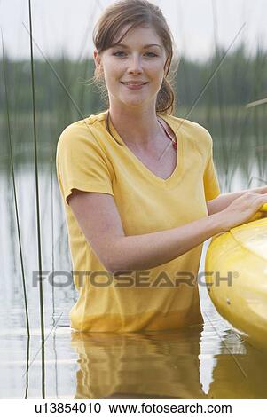 Stock Image - Young woman waist deep in lake, beside kayak on Lake Katherine, Riding Mountain National Park, Manitoba, Canada. Fotosearch