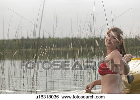 Stock Photograph - Young woman waist deep in water splashing water toward camera, Lake Katherine, Riding Mountain National Park, Manitoba, Canada. Fotosearch