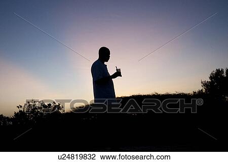 Stock Image - Silhouette of man against Kenya sky at sunset. Fotosearch