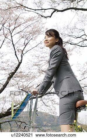 Stock Image - Businesswoman riding a bicycle in a field. Fotosearch