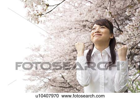 Stock Image - Businesswoman standing underneath cherry trees. Fotosearch