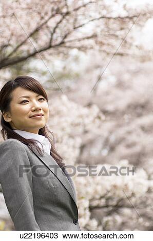 Stock Image - Businesswoman standing underneath cherry trees. Fotosearch