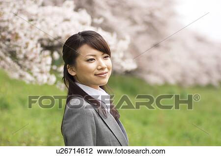 Stock Image - Businesswoman standing underneath cherry trees. Fotosearch