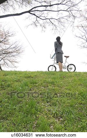 Stock Image - Businesswoman with a bicycle in a field. Fotosearch