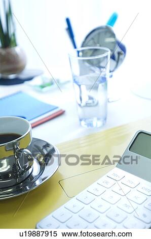 Stock Photography - Calculator, coffee and glass of water on desk. Fotosearch