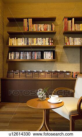 Stock Image - Chair and coffee table in front of shelves of books, DVDS and CDs. Fotosearch
