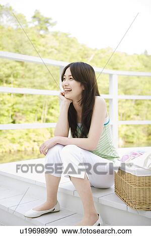 Stock Image - Cheerful young woman sitting on balcony with laundry. Fotosearch