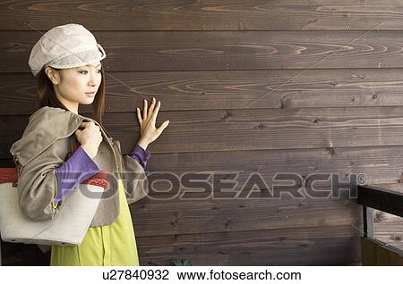 Stock Image - Fashionable woman against brown wooden wall. Fotosearch