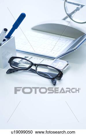 Stock Image - Glasses, pens, calculator and wristwatch on desk. Fotosearch