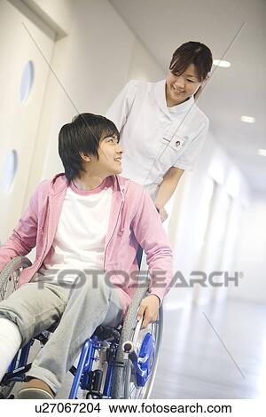 Picture - Nurse pushing patient in wheelchair along a corridor. Fotosearch