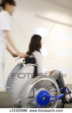 Stock Photograph - Nurse pushing patient in wheelchair along a corridor. Fotosearch