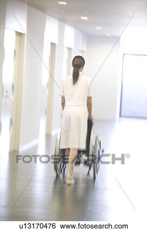 Stock Photograph - Nurse pushing patient in wheelchair along a corridor. Fotosearch