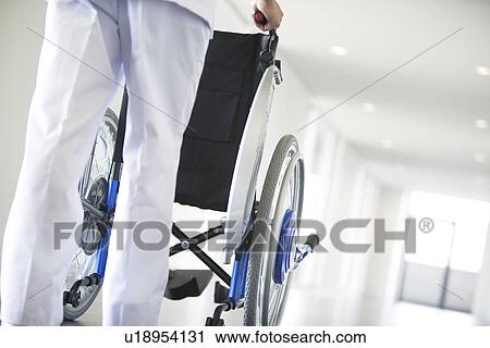 Stock Image - Orderly pushing wheelchair in hospital. Fotosearch