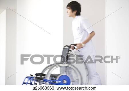 Stock Image - Orderly pushing wheelchair in hospital. Fotosearch