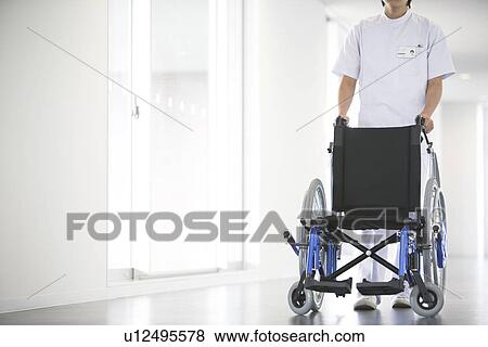 Stock Photo - Orderly pushing wheelchair in hospital. Fotosearch